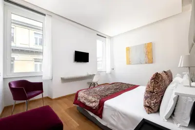 a white bedroom with a bed and a chair at Mascherino Suites in Rome