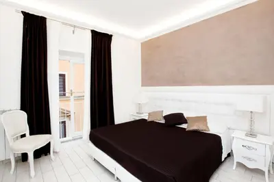 a white bedroom with a black bed and a chair at Town House Fontana Di Trevi in Rome