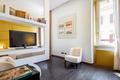 a living room with a television and a white chair at HT Romeo Al Babuino in Rome