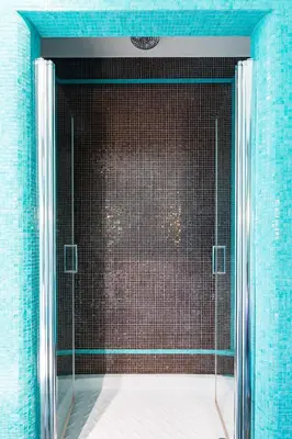 a glass shower in a bathroom with blue tiles at Rooms Roma - Monti in Rome