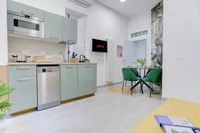 a kitchen with white cabinets and a table with green chairs at Colosseo Secret Garden - Home and More in Rome