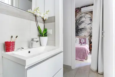 a white bathroom with a sink and a bedroom at Colosseo Secret Garden - Home and More in Rome