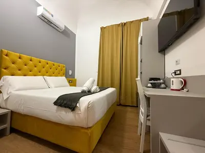 a bedroom with a bed with a yellow headboard and a desk at Conte GuestHouse in Rome