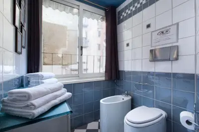 a blue tiled bathroom with a toilet and a window at Delle Grotte Apartment in Rome