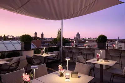 a rooftop patio with tables and chairs and a view of the city at The First Arte - Preferred Hotels & Resorts in Rome