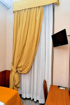 a bedroom with a yellow curtain and a television at Hotel Cervia in Rome