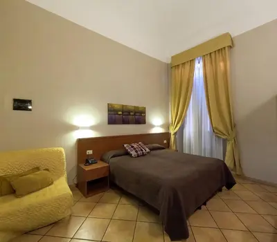 a bedroom with a bed and a chair and a window at Hotel Cervia in Rome