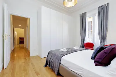 a white bedroom with a bed and a red chair at Modern Apartment Quirina 300 mt from Vatican in Rome