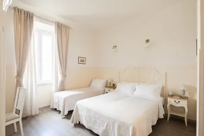 a white bedroom with two beds and a window at Dante's in Vaticano 2 in Rome