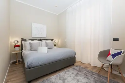 a white bedroom with a bed and a chair at 126 Gracchi Suites in Rome