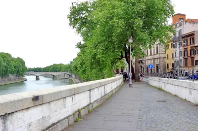a sidewalk next to a river with a bridge at the blu and green apartment in Rome