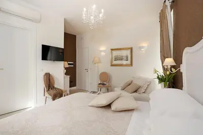 a white bedroom with a large bed and a chandelier at Daplace - HQH Colosseo in Rome