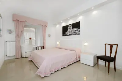 a white bedroom with a pink bed and a chair at Ludovisi Barberini Grand Apartment in Rome