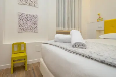 a white bedroom with a bed and a yellow chair at Many Days Apartments in Rome
