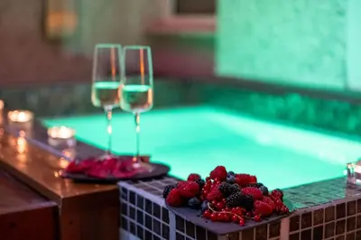 two glasses of wine and fruit next to a swimming pool at SuiteFrattini Private Spa in Rome