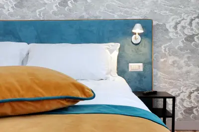a bed with a blue headboard with a pillow and a lamp at Opera 58 - Teatro dell'Opera Suites in Rome