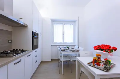 a kitchen with white cabinets and a table with red flowers at Elements Guest House Roma in Rome