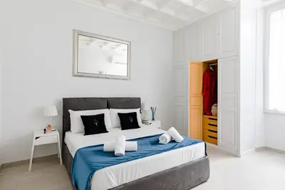a white bedroom with a large bed with blue blanket at A World Aparts - 61 Margutta in Rome