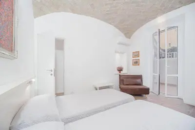 a white bedroom with two beds and a chair at groundfloor wonderfull apartment in Rome