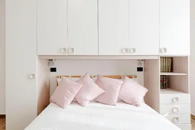 a white bed with white cabinets and pink pillows at G&C house in Rome