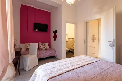 a bedroom with a pink wall with a bed and a chair at DOMUS FORTUNAE VATICANO in Rome