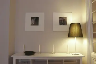 a table with a lamp and some pictures on the wall at Roman Suite in Rome