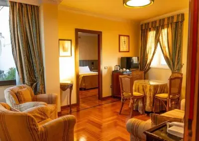 a living room with a table and a bedroom at Hotel Mecenate Palace in Rome