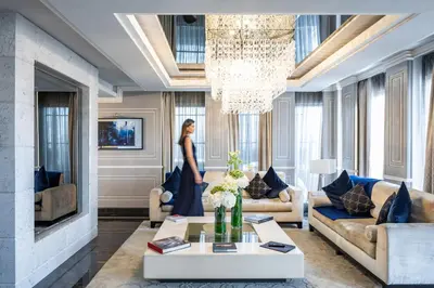 a woman standing in a living room with a chandelier at Baglioni Hotel Regina - The Leading Hotels of the World in Rome