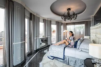 a woman sitting on a bed in a room with windows at Baglioni Hotel Regina - The Leading Hotels of the World in Rome