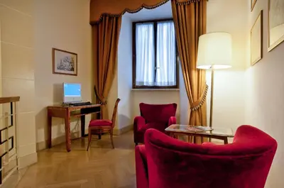 a living room with red chairs and a desk with a computer at Bettoja Hotel Atlantico in Rome