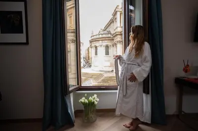 a woman in a white robe looking out of a window at The Major Hotel in Rome