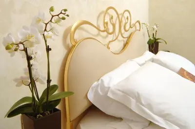 a bedroom with a white bed with a gold headboard at Residenza Frattina in Rome