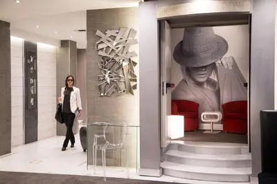a woman walks past a large painting of a woman wearing a hat at Hotel Ariston in Rome