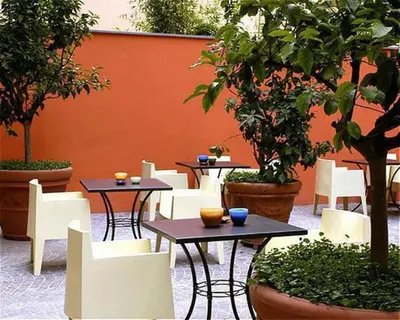 a patio with tables and white chairs and trees at Hotel Abitart in Rome