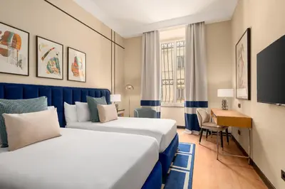 a hotel room with two beds and a desk at Room Mate Collection Mia, Rome Colosseum in Rome