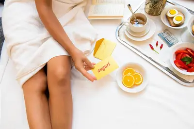 a woman in a white dress sitting on a bed with food at Yes Hotel Boutique Rome in Rome