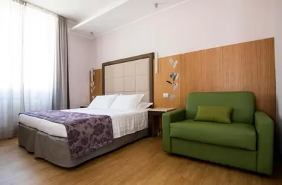 a bedroom with a bed and a green chair at Hotel Giolli Nazionale in Rome