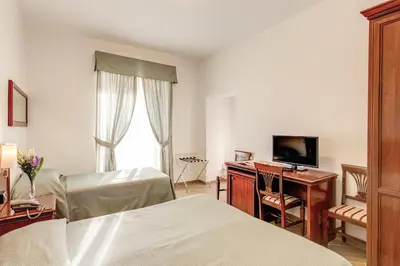 a bedroom with two beds and a desk and a television at Hotel Flavio in Rome