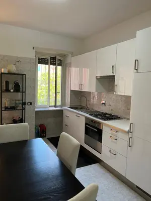 a kitchen with white cabinets and a table and a refrigerator at Red house in Monteverde - Cale 02 in Rome