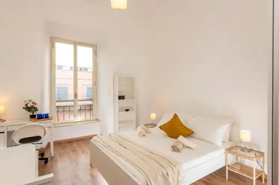 a white bedroom with a bed and a desk and a window at Bell Appartamento in Rome