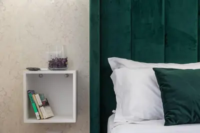 a white night stand next to a bed with a green headboard at Portico d'Ottavia LUX in Rome