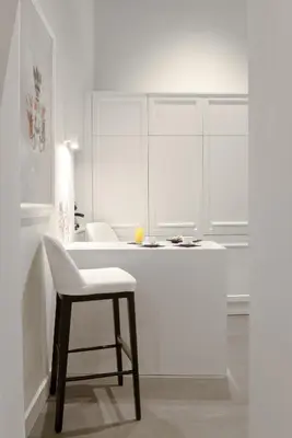 a white kitchen with a white counter and a chair at Carthusia Suites Roma in Rome